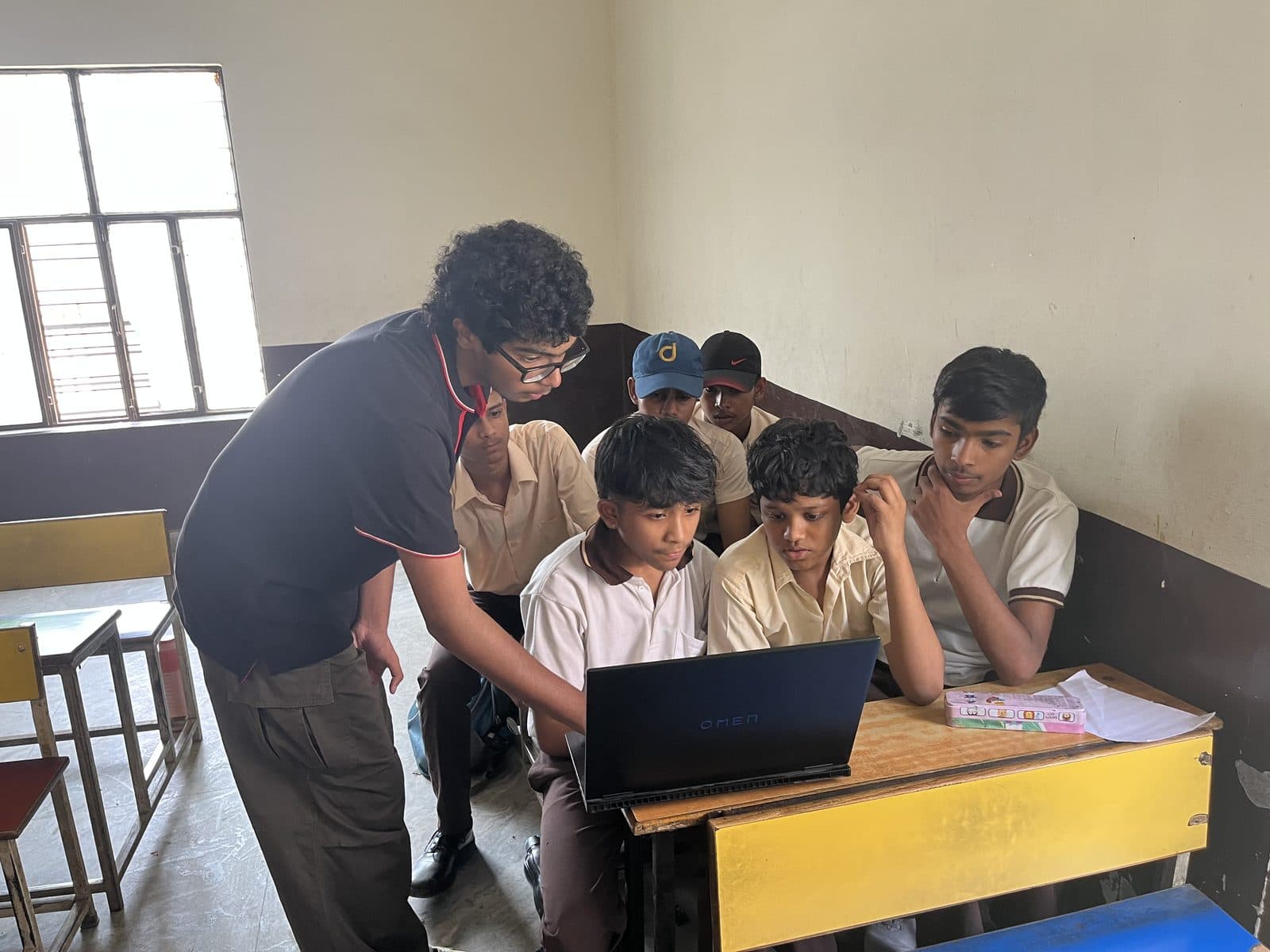 A member of the Edugram team showing three seated students the Edugram site on a laptop at their desk.