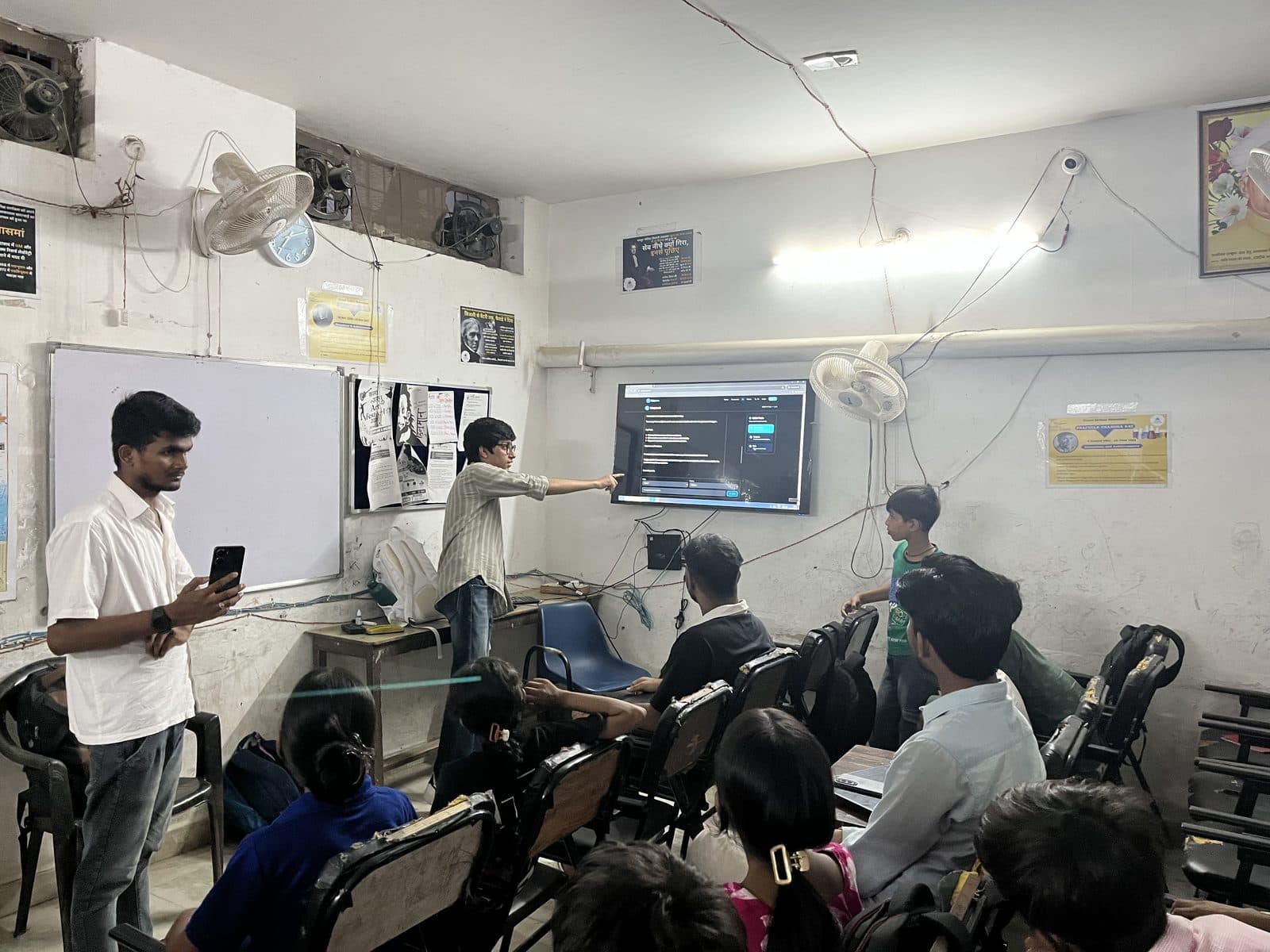 Students seated at Prayatna watching the Edugram site on a wall-mounted screen during the evening session.